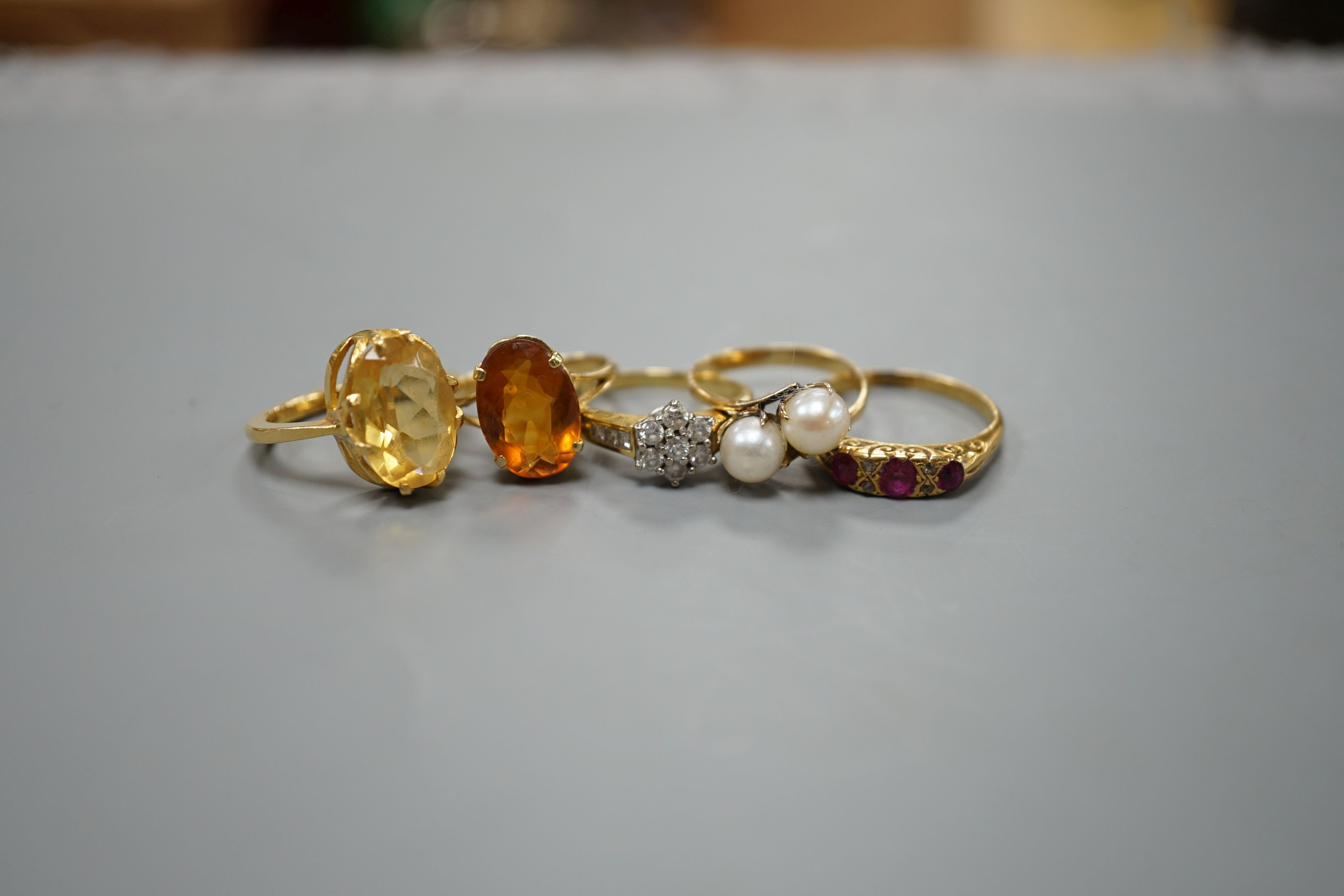 Five assorted gold and gold coloured metal dress rings, comprising a two stone cultured pearl stamped 18k, size L, an 18ct gold diamond cluster, size L, an unmarked citrine?, an 18ct orange stone, size L and an early 20t